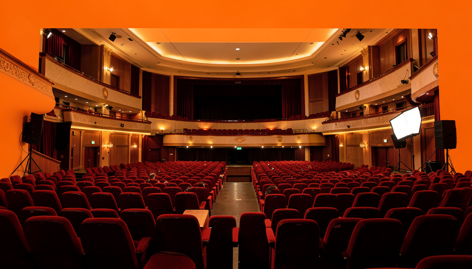 A warm atmospheric photograph of a concert hall interior with soft golden lighting and rich red seating