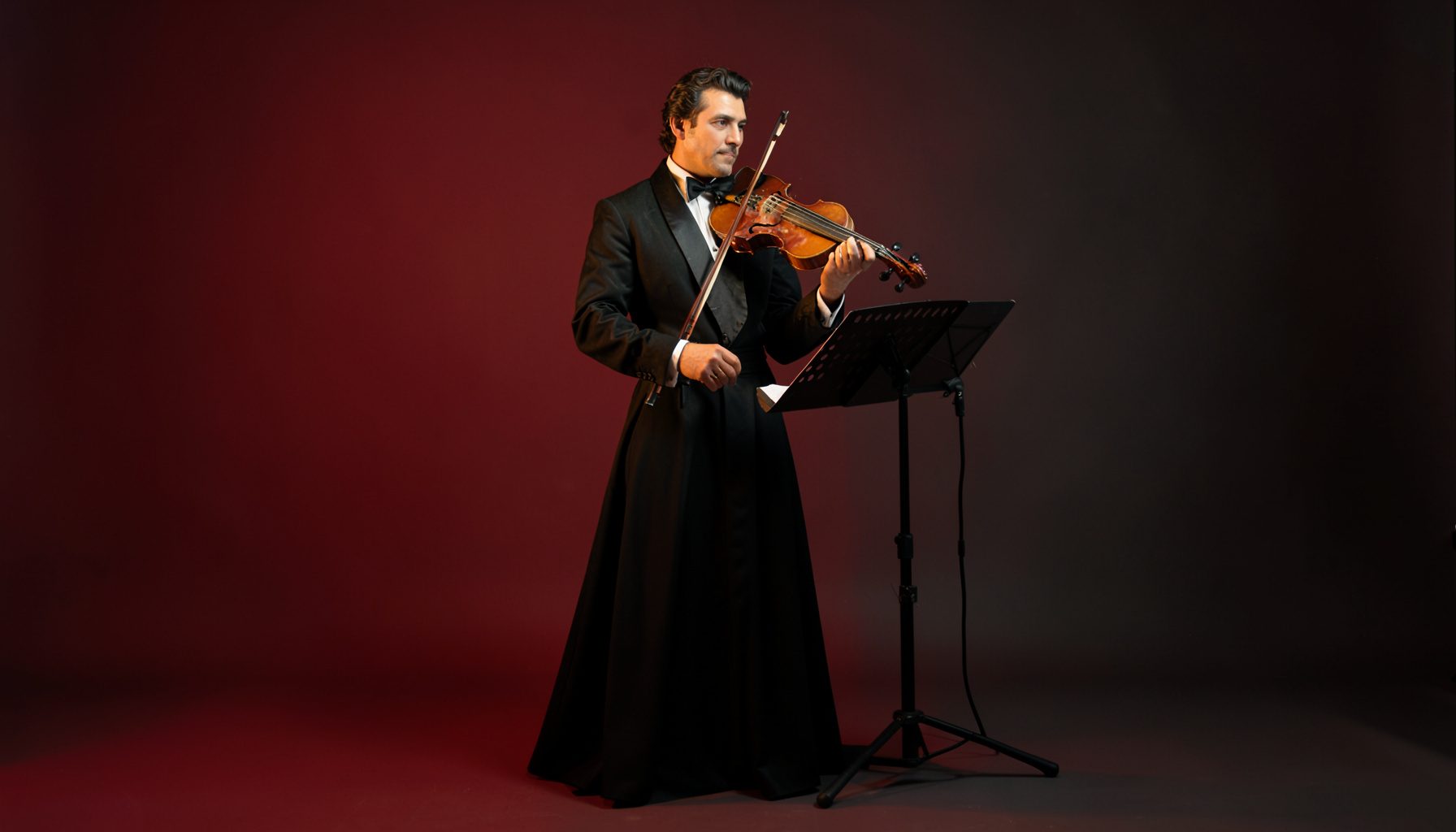 A violinist in a formal gown beside a music stand, warm golden light falling across the instrument