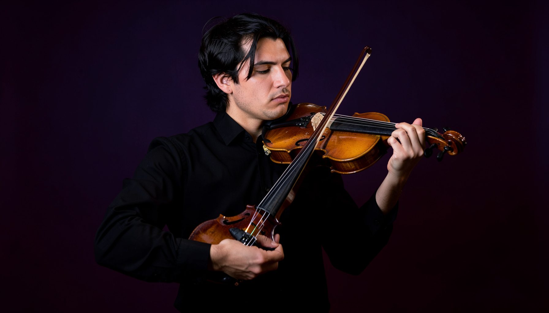 A violinist holding an electric violin against a deep indigo backdrop, dramatic side lighting