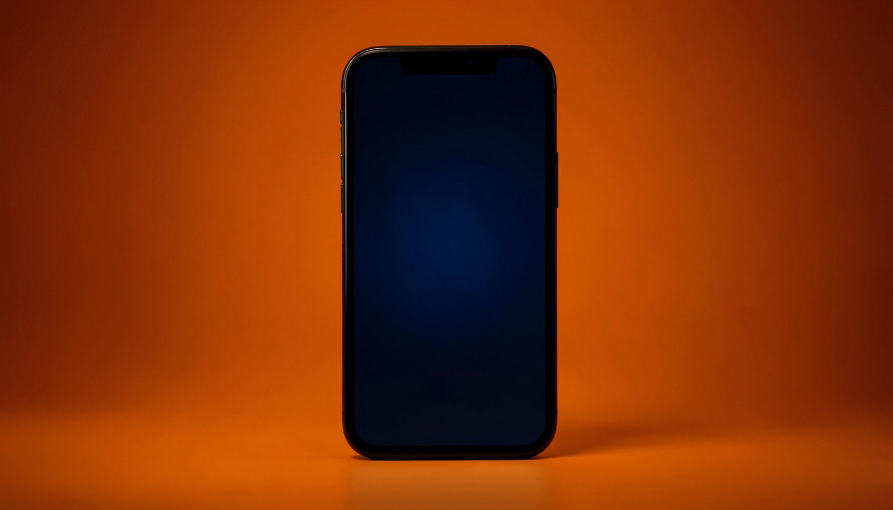 A dark atmospheric photograph of a smartphone screen glowing against a dim concert-hall background, with warm amber and deep navy tones