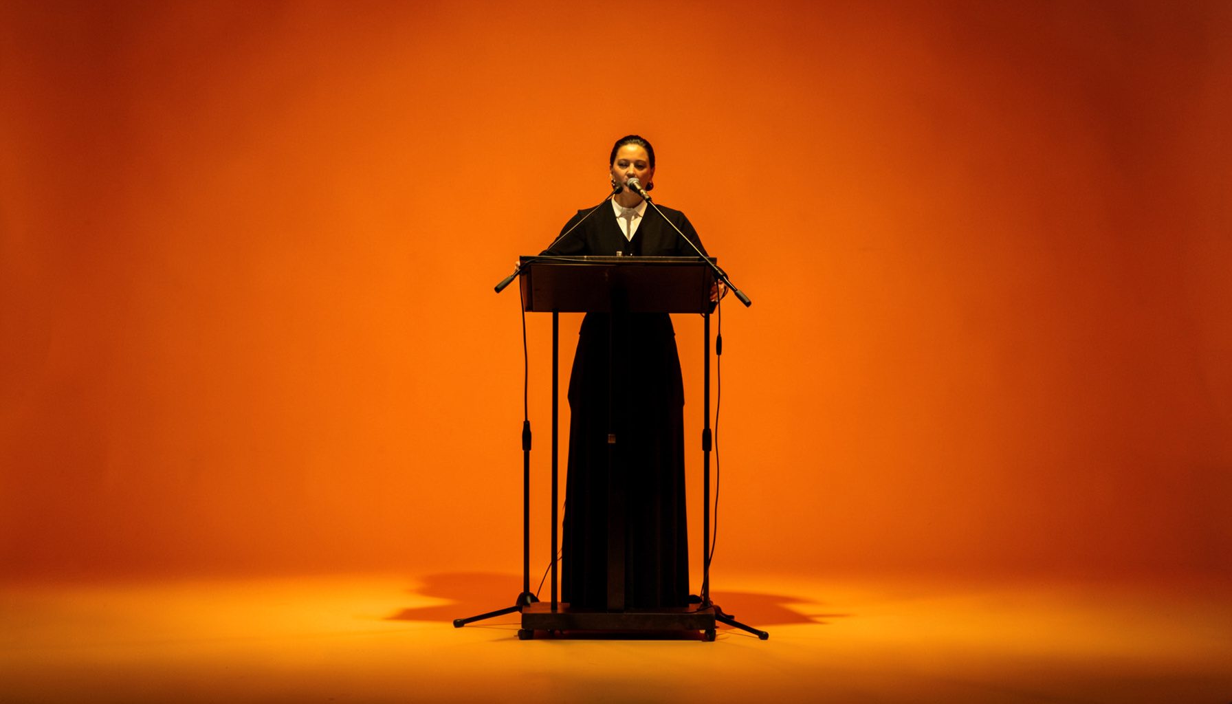 A conductor's podium and music stand on an empty stage, bathed in soft amber light with deep shadows