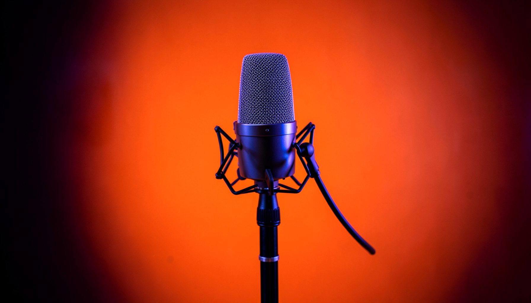 A microphone on a studio stand against a dark backdrop with subtle purple and blue ambient light
