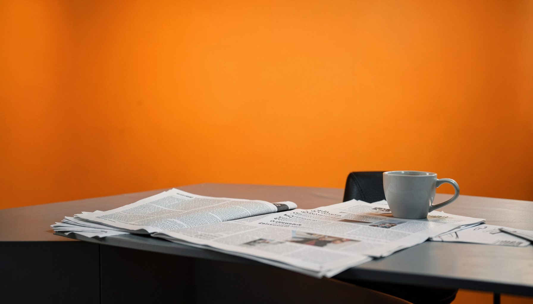 A softly lit newsroom desk with scattered newspapers and a coffee cup, in muted grays and warm amber tones
