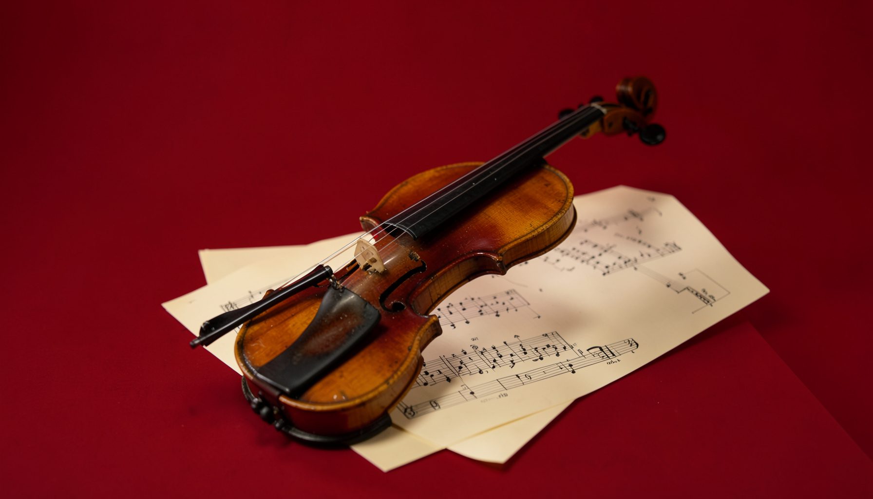 A classical violin resting on sheet music against a warm cream backdrop, with soft shadows and a refined, intimate studio atmosphere
