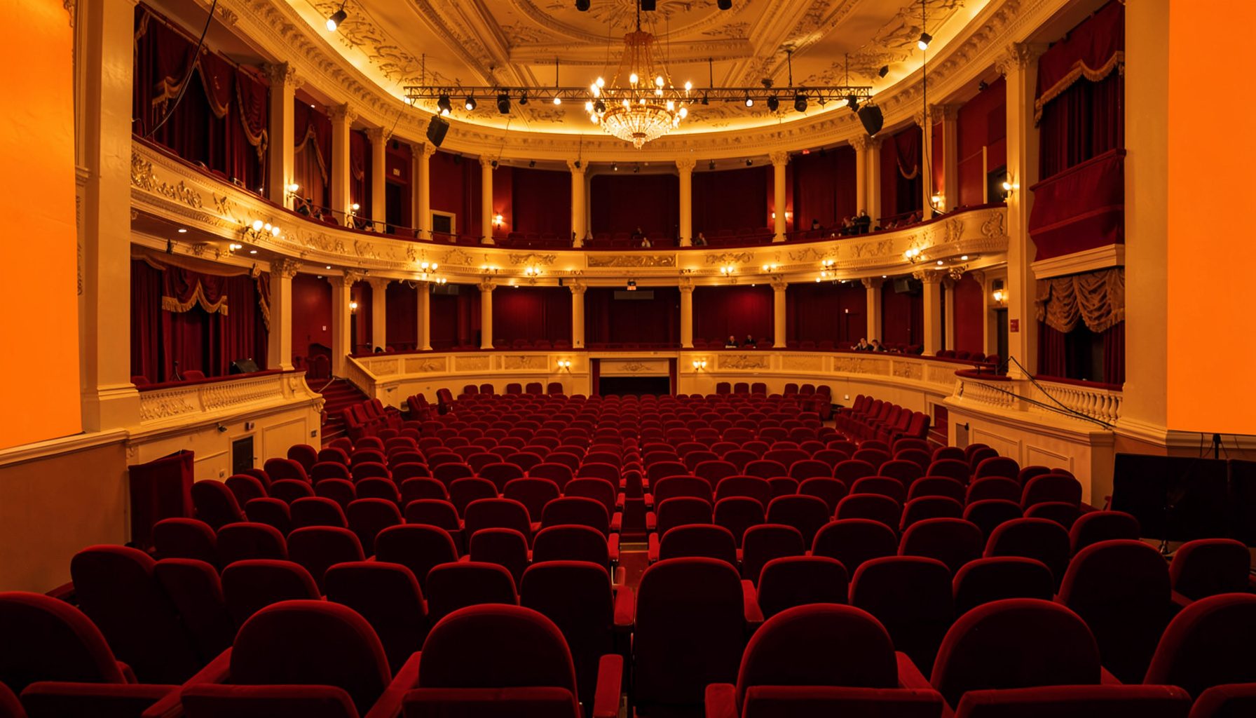 A warm atmospheric photograph of a concert hall interior with soft golden lighting and rich red seating, conveying classical music heritage